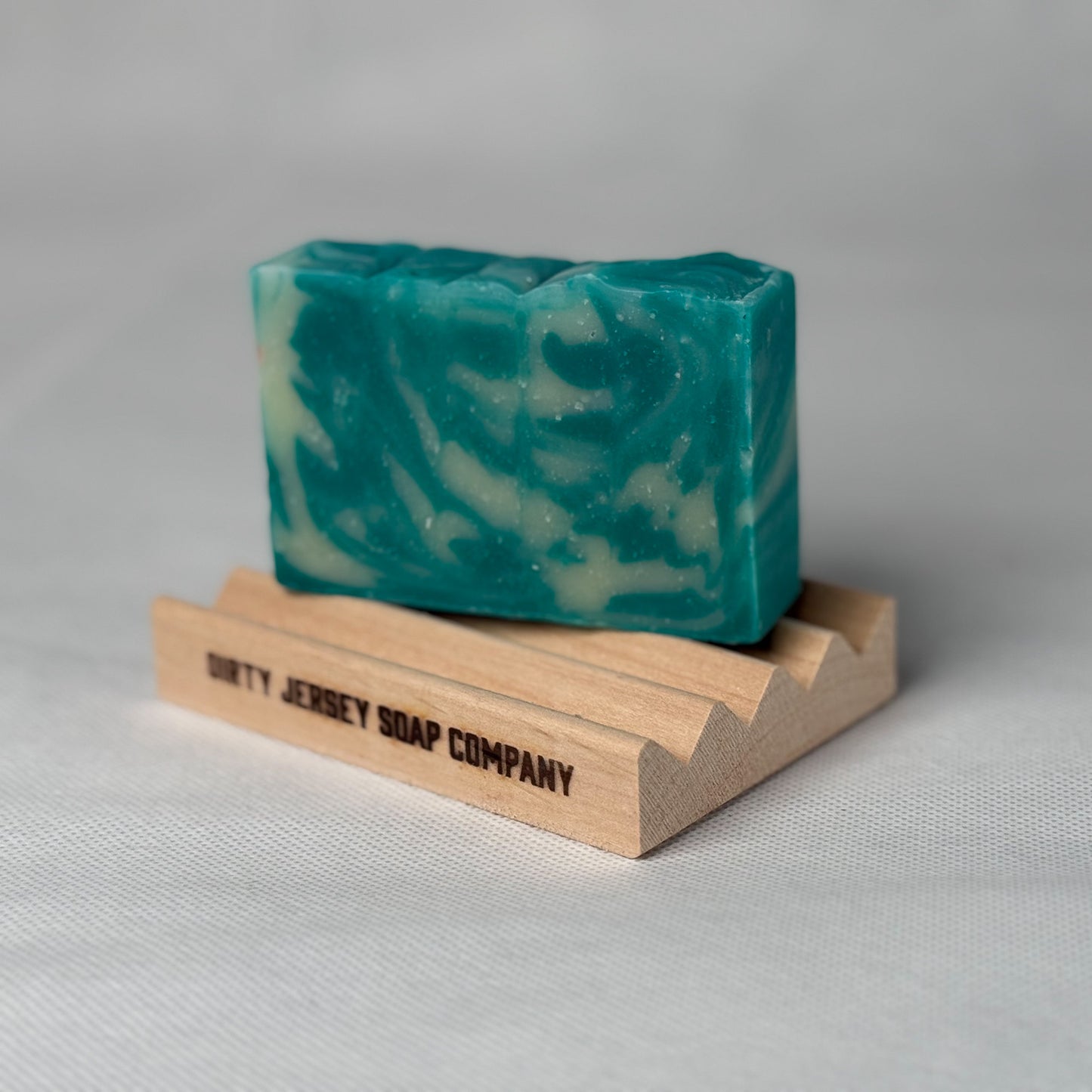 Green and white swirled soap bar on a wooden stand with 'Dirty Jersey Soap Company' branding.